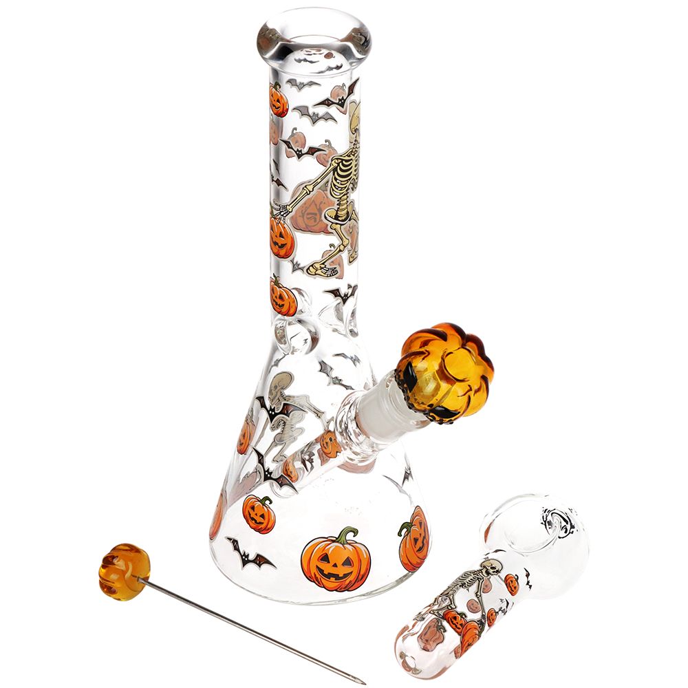 Clear glass water pipe with Halloween-themed printed designs of pumpkins, bats, and skeletons, featuring an amber glass bowl and accessories on a white background.