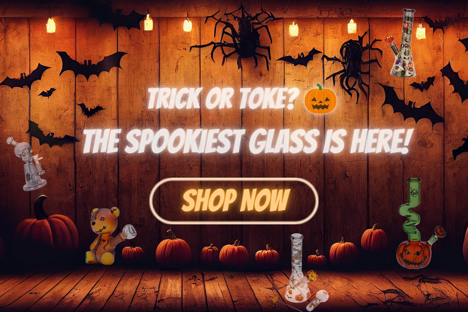 Halloween-themed promotional graphic with the text 'TRICK OR TOKE? THE SPOOKIEST GLASS IS HERE!' and a large 'SHOP NOW' button. The scene shows a wood-paneled background with hanging bulbs, black spider Bong and bat cutouts, Glass Water pipes with pumpkins, a small bong teddy bear, and several decorative glass containers, including a green glass bong and a clear Dab rig with a skull stopper.