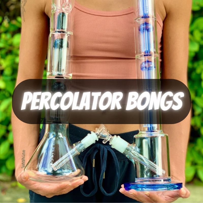 Person holding two glass percolator bongs with a green outdoor background